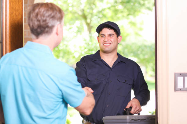 Latin descent repairman, technician makes house call at customer home. Latin descent repairman arrives at customer's front door to make requested home repairs. He wears a blue uniform and holds toolbox as they shake hands. Mature man greets repairman. door repairman men manual worker stock pictures, royalty-free photos & images