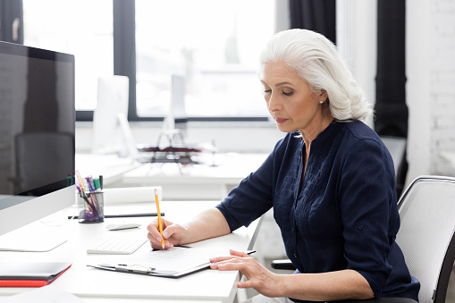Mature business woman making notes on a piece of paper at her desk