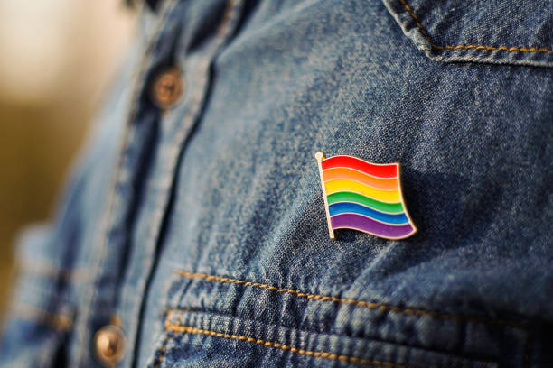 nahaufnahme eines lgbt-pins in form einer flagge ist auf blaue jeansjacke gepinnt. lgbt-rechte-konzept. - sexual issues stock-fotos und bilder