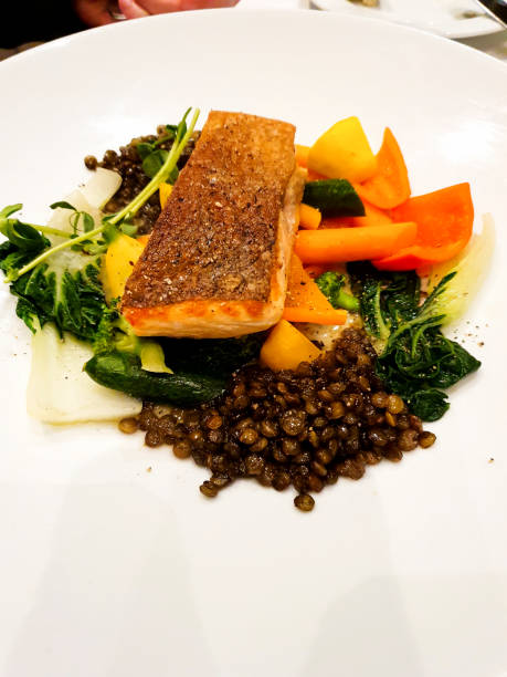 Grilled Butterfly salmon steak with cherry tomatoes and arugula salad on a black square plate. Black plate for serving the dish. Close-up.
