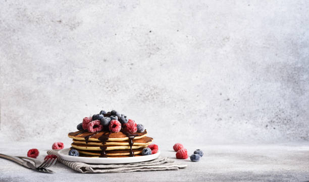 Pancakes with raspberries and blueberries and chocolate sauce for breakfast, on a concrete light background stock photo
