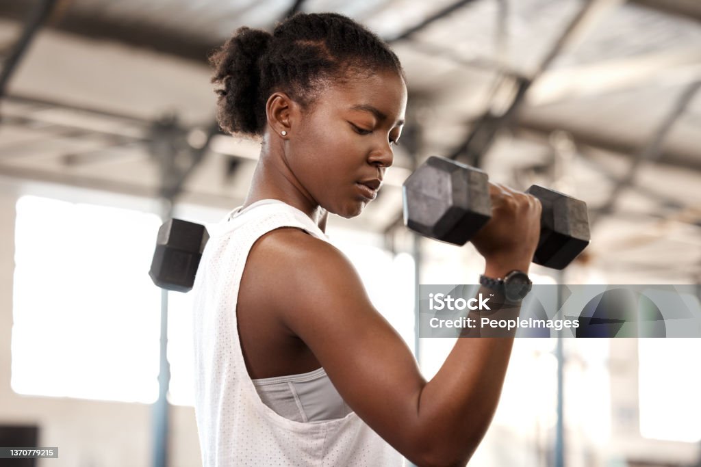 Shot of a sporty young woman exercising with a dumbbell in a gym Struggles don't define you, they refine you Women Stock Photo