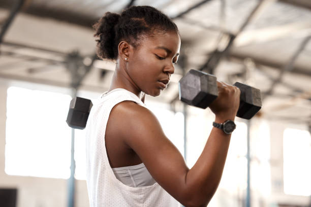 shot of a sporty young woman exercising with a dumbbell in a gym - curled up imagens e fotografias de stock