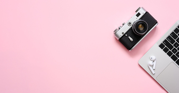 Vintage camera and silver laptop on a pink background. Flat lay, copy space.