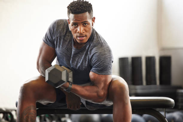 retrato de un joven musculoso haciendo ejercicio con una mancuerna en un gimnasio - levantamiento de pesas fotografías e imágenes de stock