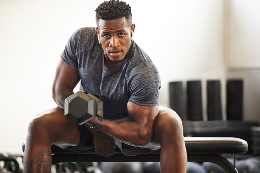 Portrait of a muscular young man exercising with a dumbbell in a gym