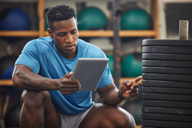 Shot of a muscular young man using a digital tablet while checking equipment in a gym Making sure all the weights are in place gym men africa muscular build stock pictures, royalty-free photos & images