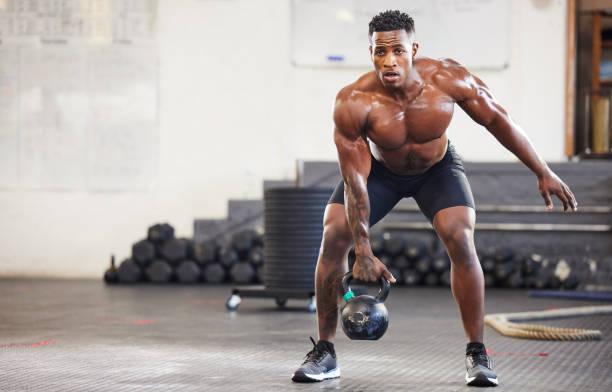 aufnahme eines muskulösen jungen mannes, der mit einer kettlebell in einem fitnessstudio trainiert - bodybuilding stock-fotos und bilder