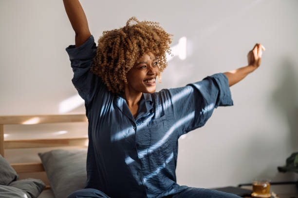 retrato de una mujer feliz que se despierta y se estira en la cama - despertar fotografías e imágenes de stock