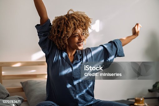 istock Portrait of a Happy Woman Waking Up and Stretching in Bed 1370783671