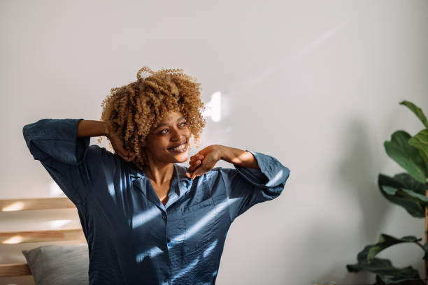 portrait of a happy woman waking up and stretching in bed - wake up stretching women black imagens e fotografias de stock