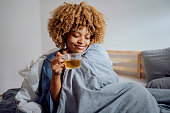 Beautiful Woman in Bed Snuggled Under the Covers Enjoying a Cup of Tea