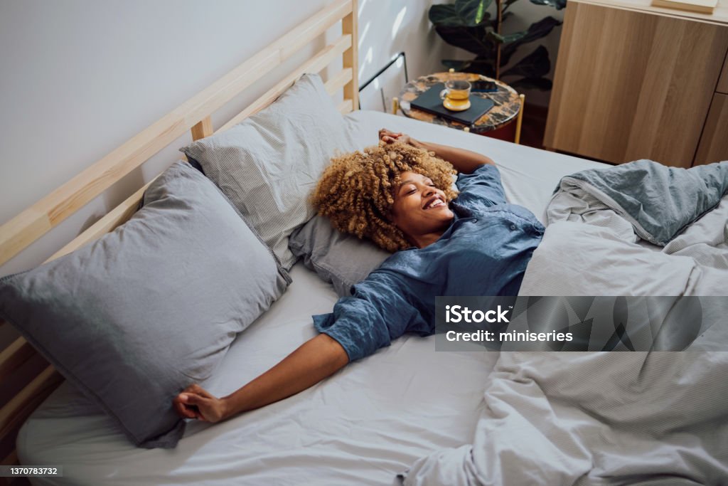 Beautiful Cheerful Woman Having a Lazy Weekend in Bed Woman is lying in her bed in the morning. She is stretching and smiling. Sleeping Stock Photo