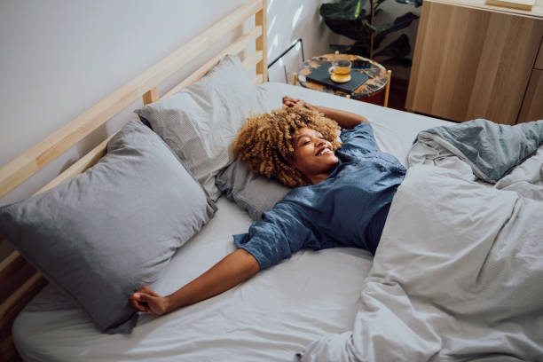 Beautiful Cheerful Woman Having a Lazy Weekend in Bed Woman is lying in her bed in the morning. She is stretching and smiling. pajamas stock pictures, royalty-free photos & images