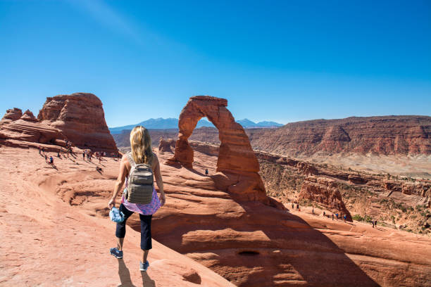 Woman hiker enjoying beautiful red mountain scenery  in Utah. Woman relaxing on summer vacation hiking trip enjoying beautiful red mountain scenery. Girl hiker standing on top of the mountain looking at view. Delicate Arch, Moab, Utah, Arches National Park, USA delicate arch stock pictures, royalty-free photos & images