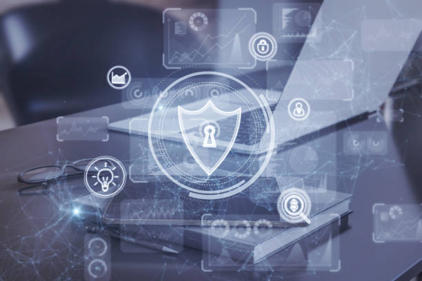 istock Close up of desktop with laptop, other items and creative glowing protection shield with polygonal mesh connections and business icons. Safety, security and communication concept. Double exposure. 1370787585