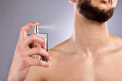 A man holds a clear bottle of cologne eau de toilette spray and applies it to his neck area.