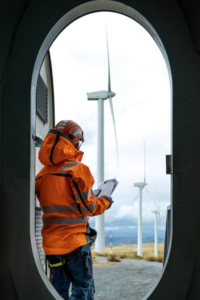 travailleur avec une veste orange dans un parc éolien - working windmill photos et images de collection