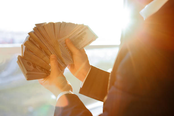Good looking young man in full suit counting money and smiling while standing against
