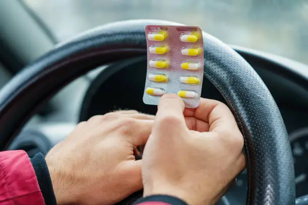 Blister of pills in the hands of the driver on a blurred background of the steering wheel in the car. The use of pharmacological drugs for medical purposes while driving. Selective focus