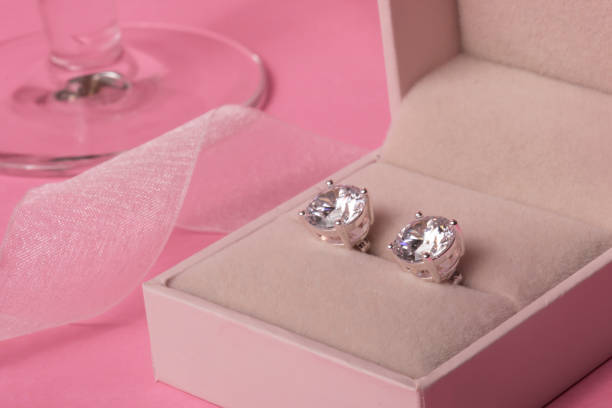 Diamond earrings in jewel box with champagne glass and ribbon on a pink background stock photo