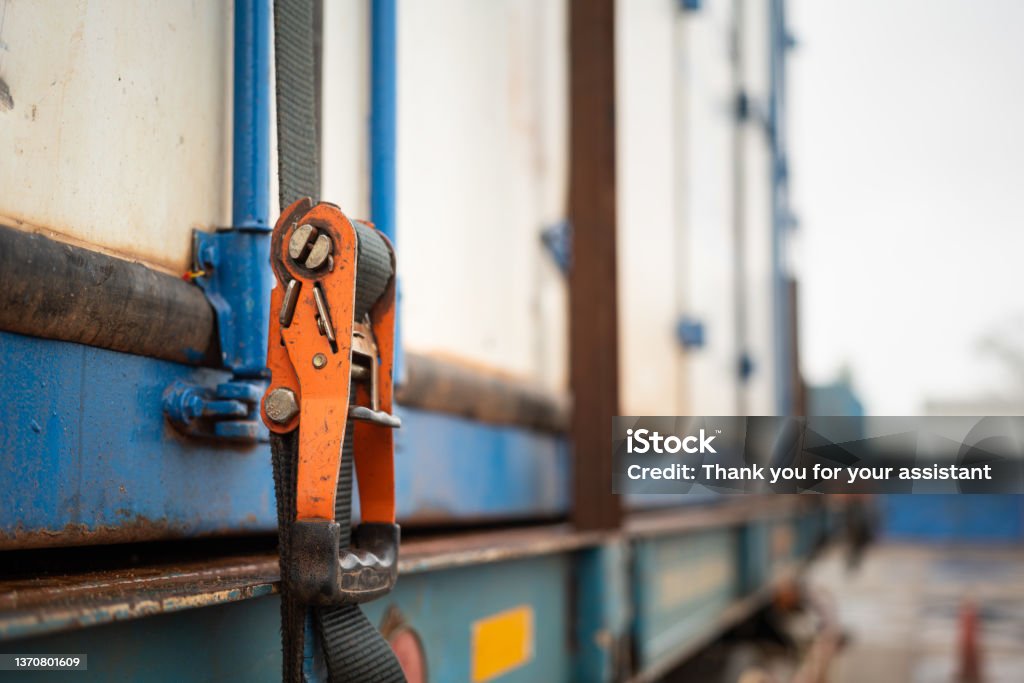 Cargo strap lashing on container - safety in transportation. Webbing belt strap lashing to secure container or load which is prepared for transport on the truck. Safety in transportation industrial scene photo. Close-up and selective focus at the object part. Cargo Container Stock Photo