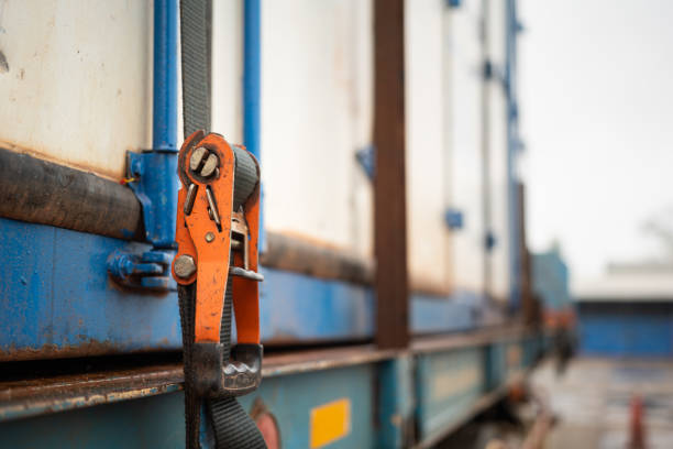 Cargo strap lashing on container - safety in transportation. Webbing belt strap lashing to secure container or load which is prepared for transport on the truck. Safety in transportation industrial scene photo. Close-up and selective focus at the object part. restraining device stock pictures, royalty-free photos & images