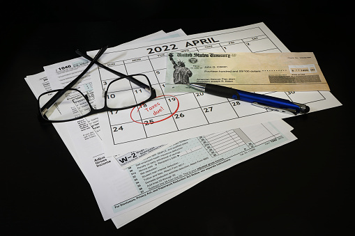 Concept of 2021 Tax preparation documents and a calender with April 18th circled the words Taxes Due circled in red. On black background.