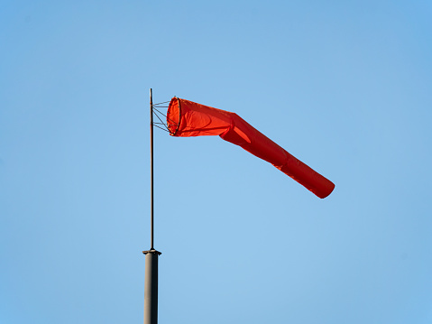 White and red wind flag (windsock)at the harbour of Spiekeroog, East Frisian Island, Germany. Air sleeve on a sunny day indicating direction of wind. Windy weather concept.