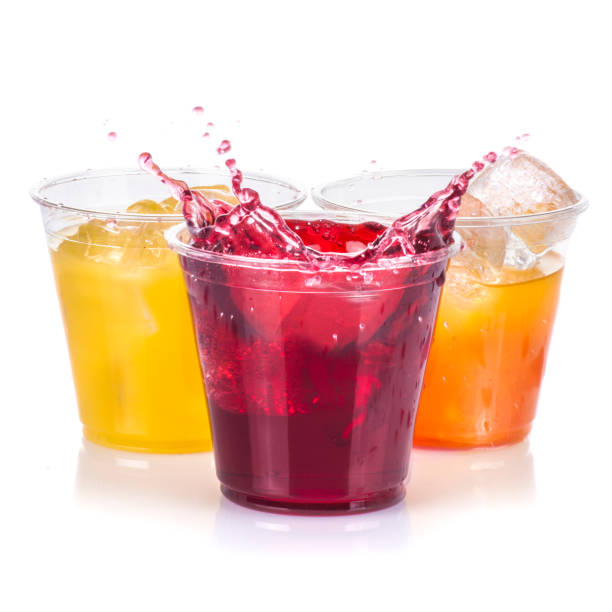 istock Clear plastic cups with red yellow and orange juice drinks splashing from ice cube on white background 1370816532