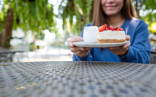 Closeup image of a young woman holding and serving a piece of strawberry cheese cake in a plate