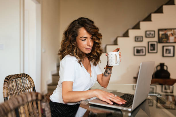 istock Woman drinking a cup of coffee while working on a laptop at home. 1370820352