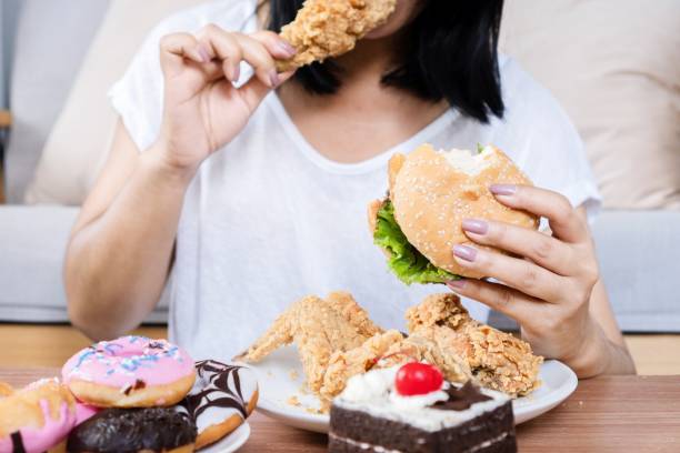 concept de trouble de l’hyperphagie boulimique avec une femme mangeant un hamburger de restauration rapide, du poulet cuit, des beignets et des desserts - matière grasse aliment photos et images de collection