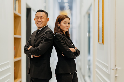 Confidence Malay businessman and businesswoman arms crossed in office corridor and smiling at camera