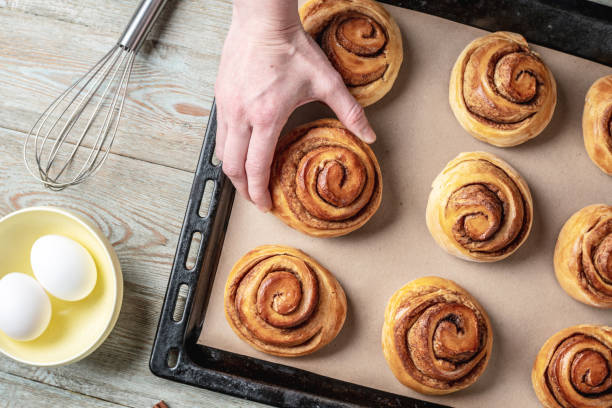 istock Woman hands are carefully taking out fresh warm cinnamon rolls buns from a baking tray. Concept of delicious homemade pastry and cozy atmosphere 1370831159