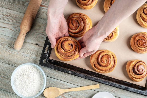 istock Woman hands are carefully taking out fresh warm cinnamon rolls buns from a baking tray. Concept of delicious homemade pastry and cozy atmosphere 1370831161