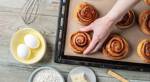 istock Woman hands are carefully taking out fresh warm cinnamon rolls buns from a baking tray. Concept of delicious homemade pastry and cozy atmosphere 1370831163