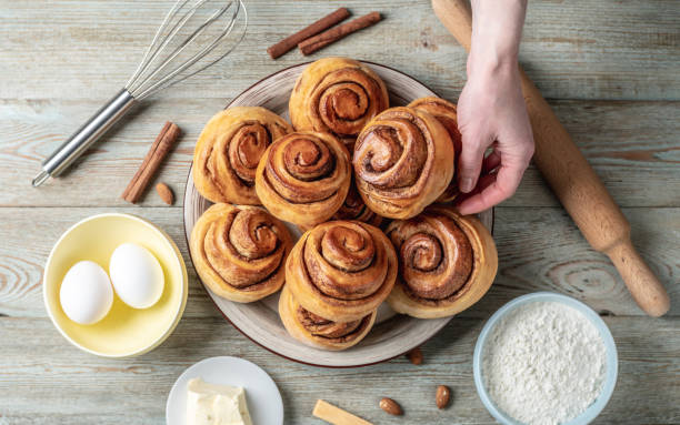 istock Hand is gently picking up a fresh cinnamon roll from a plate full of buns. Concept of delicious homemade pastries and a cozy atmosphere. Top view 1370831170