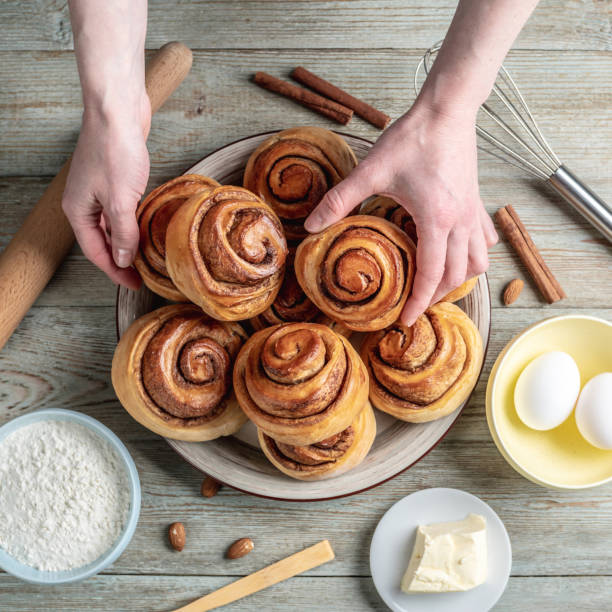 istock Hand is gently picking up a fresh cinnamon roll from a plate full of buns. Concept of delicious homemade pastries and a cozy atmosphere. Top view 1370831171
