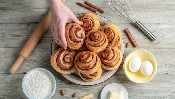 istock Hand is gently picking up a fresh cinnamon roll from a plate full of buns. Concept of delicious homemade pastries and a cozy atmosphere. Top view 1370831174