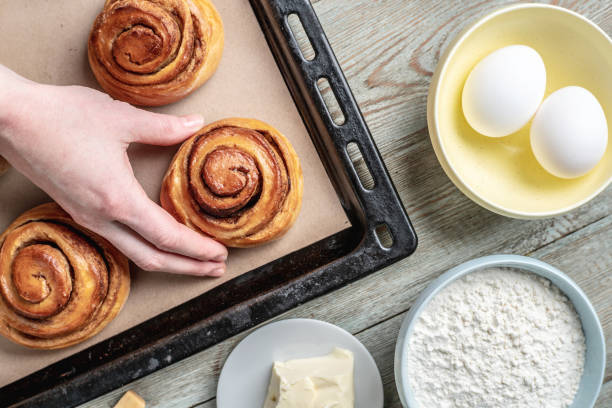istock Woman hands are carefully taking out fresh warm cinnamon rolls buns from a baking tray. Concept of delicious homemade pastry and cozy atmosphere 1370831189