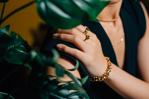 Closed up of golden ring and bracelet on the women's hand with green plant leaf.