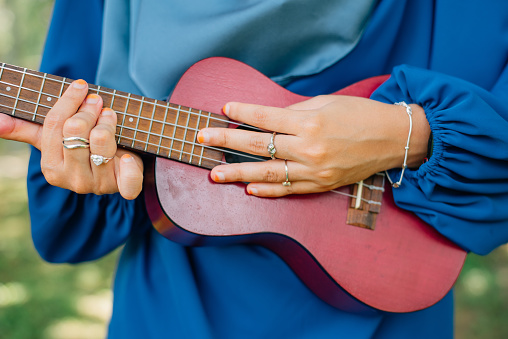 Fashionable woman with luxury accessories such as diamond ring and silver bracelet while playing with ukulele outdoor
