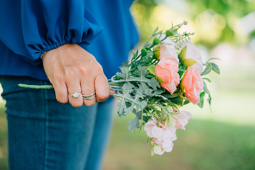 Fashionable woman with luxury accessories such as diamond ring and silver bracelet while holding a bouquet of flowers outdoor.
