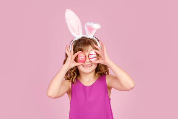 istock Delighted child covering eye with eggs during Easter party in pink studio 1370836241