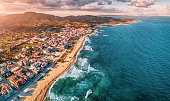 Dramatic panoramic aerial view of iconic Sarti resort town and famous long and empty sandy beach at sunset time with high waves. Vacation on Halkidiki, Greece