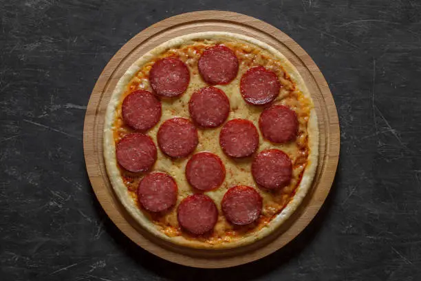 Photo of Pepperoni pizza with sausage, whole uncut, top view dark background.