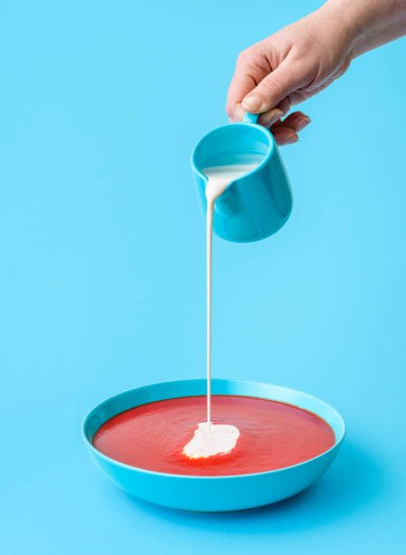 Pouring cream in tomato soup minimalist on a blue background