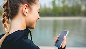 Young girl making sport in the park using mobile phone and wireless headphones