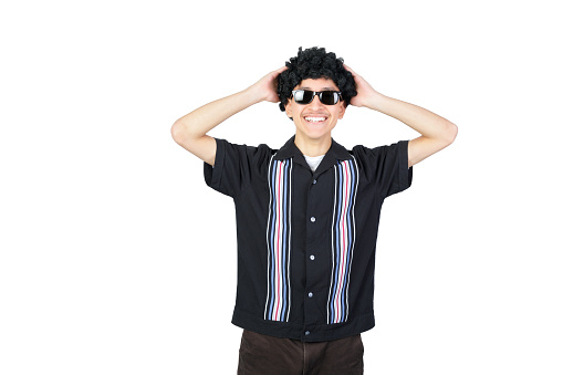 Handsome guy smiling looking at camera with her hands in the head, wearing an afro wig and sunglasses. Isolated on white background. Latin 18-20 years old guy.